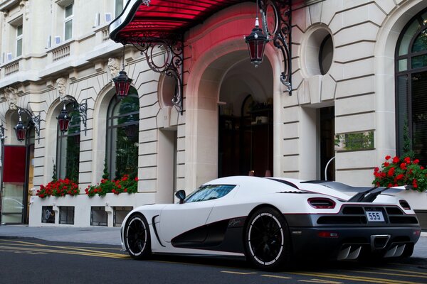 Ein weißer koenigsegg steht mit roten Blumen am weißen Haus