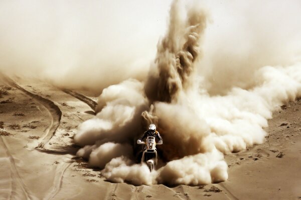 Motociclista cavalca nel deserto accelerando la sabbia in diverse direzioni con un enorme colonna di fumo