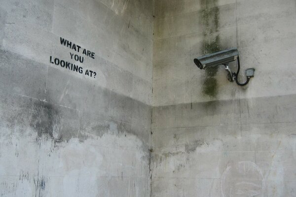 A gray wall with a camera and an inscription