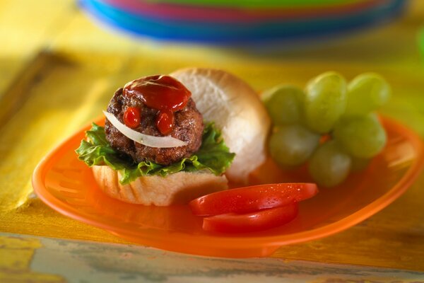 Sandwich mit Brötchen, Tomaten und Ketchup, neben Trauben