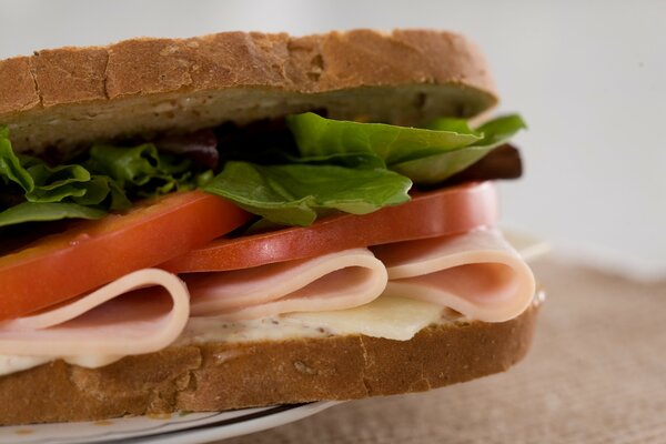 Schmackhaftes Sandwich mit Salat, gut zubereiteten Tomaten und gut zubereitetem Schinken