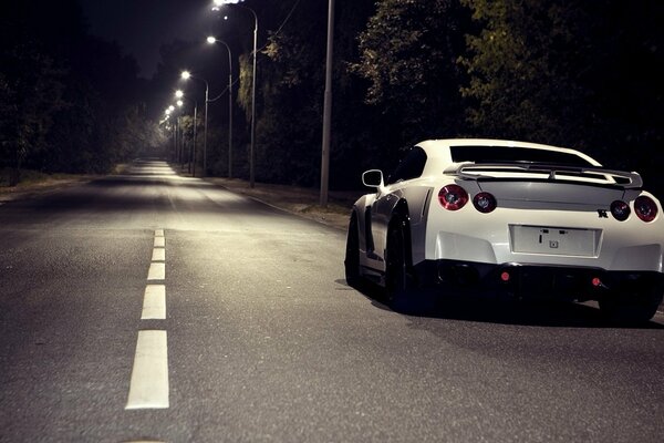 A white car is moving on a night and empty road