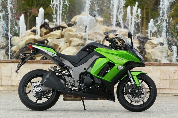 A black and green motorcycle stands next to the fountain