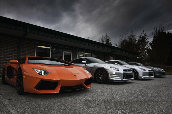 Voitures de marques Lamborghini, Aventador, Nissan sur fond de bâtiment et de ciel gris dans les nuages