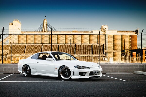 A white tuned Nissan is parked crookedly in the parking lot