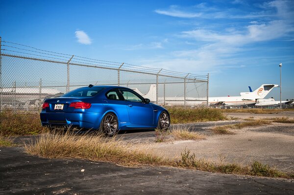 Blauer BMW auf dem Hintergrund von Fechten und Flugzeugen 