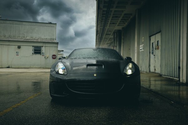 A black Ferrari divided by rays of light against the background of the industrial zone 