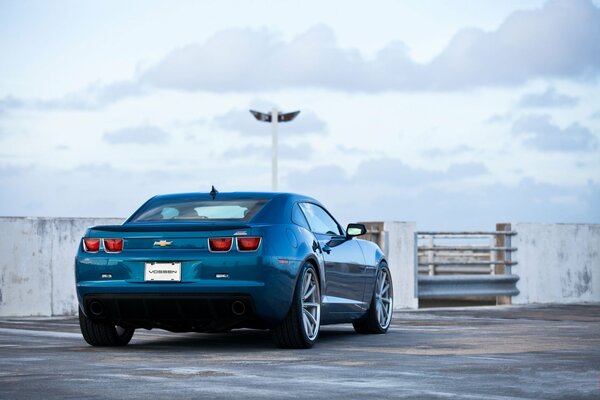 Niebieski chevrolet Camaro ss na parkingu wśród białego nieba, na którym unoszą się białe chmury