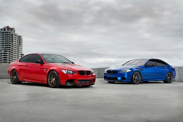 Two red and blue BMW cars standing on the roof of a building against a cloudy sky