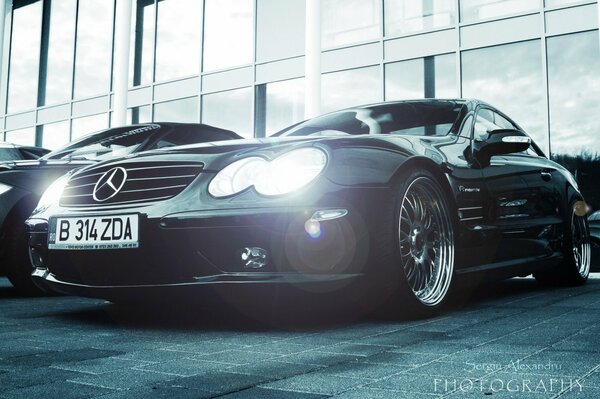 A Mercedes car with its headlights on is standing on the street