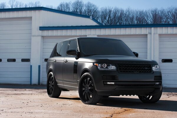 El Land Rover negro mate con ventanas tintadas se encuentra junto a los garajes