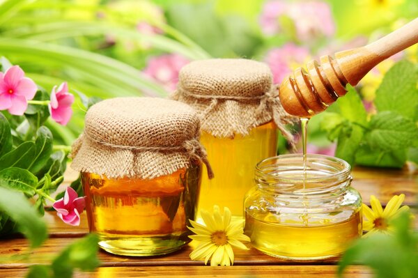 Yellow honey dripping from a spoon on a background with flowers