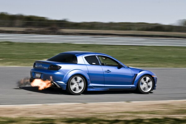 A blue Mazda is racing on the highway with fire from the exhaust pipe