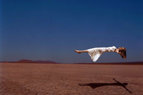 A girl in a white dress hovering over the desert