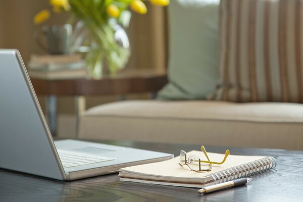 Sur la table se trouve un ordinateur portable avec un bloc-notes et un stylo