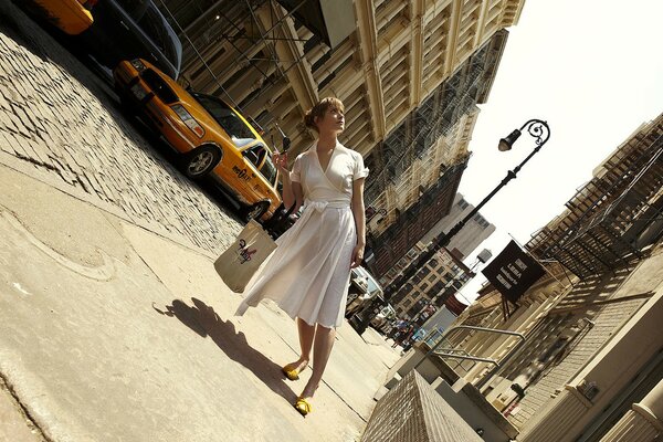 Fille en robe blanche dans la rue sur fond de taxi