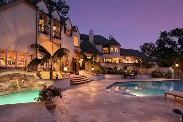 The house is lit by lanterns with a swimming pool on the background of the evening sky