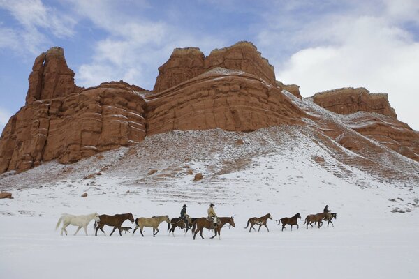 Cowboys drive horses along a snow-covered trail