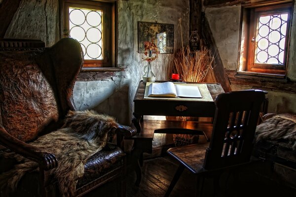 The corner of the room in which we see an armchair, a chair and an open book on the desk