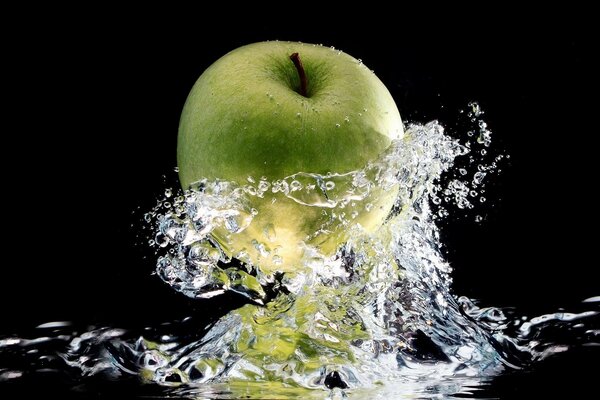 Manzana verde en salpicaduras de agua sobre fondo negro