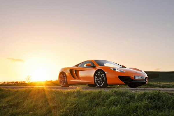 Wallpaper with a bright orange mclaren mp4-12c on the background of the setting sun