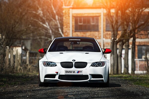 Bmw blanco en la carretera contra el fondo de los árboles y la casa