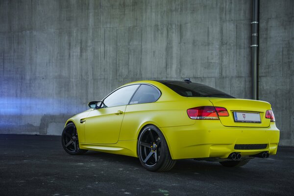 Coche amarillo de dos puertas contra un muro de hormigón