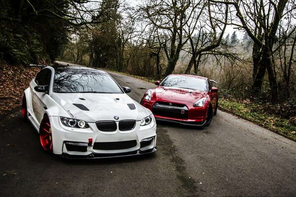 BMW blanco y Nissan rojo en el camino de otoño del bosque