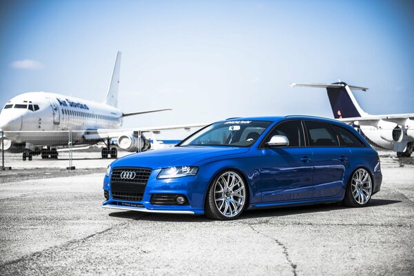 Audi A4 azul en el campo de despegue con aviones