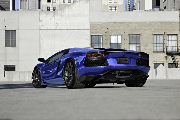 A blue sparkling Lamborghini lp700-4 on the asphalt near a gray building with windows