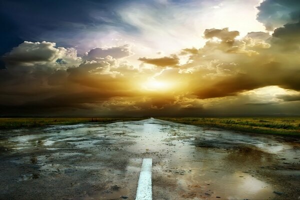 A road with puddles at sunset and reflection of clouds