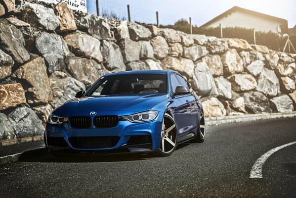 Bmw sintonizzata blu in curva su uno sfondo di recinzione in pietra