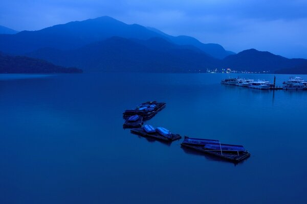 A couple of boats are standing in the bay at night against the background of mountains and lights of the opposite shore