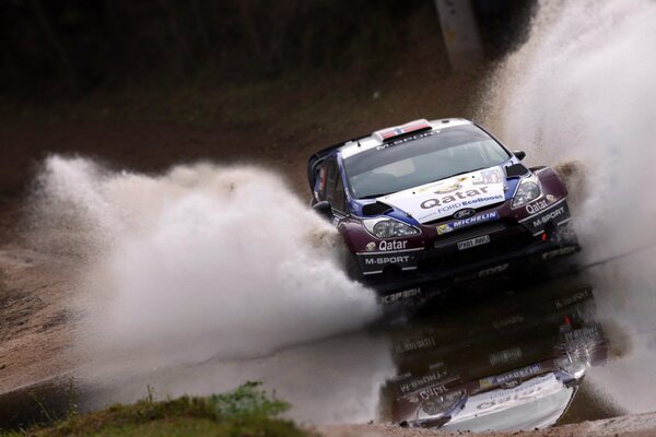 A car drives through a huge puddle during a competition