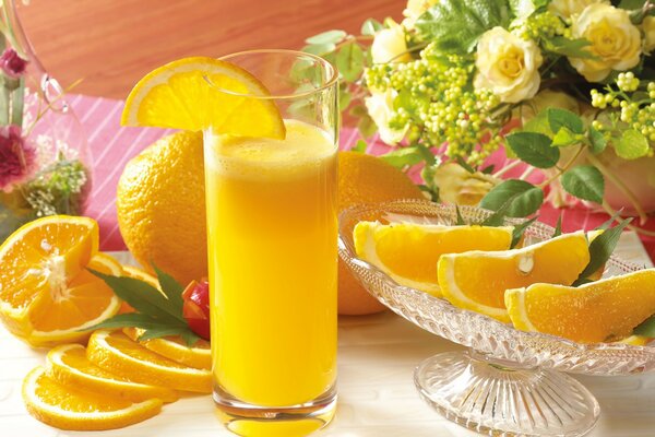 Vaso de jugo de naranja y rodajas de naranja en un jarrón