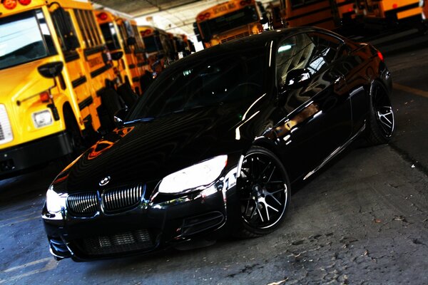 Black BMW on the background of school buses