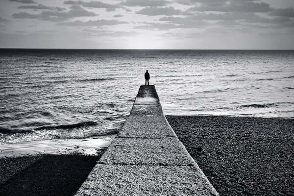 Fondo blanco y negro, un hombre en un muelle que se adentra en el horizonte