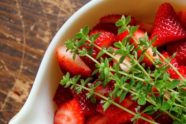 Strawberries in a white bowl with sprigs of grass