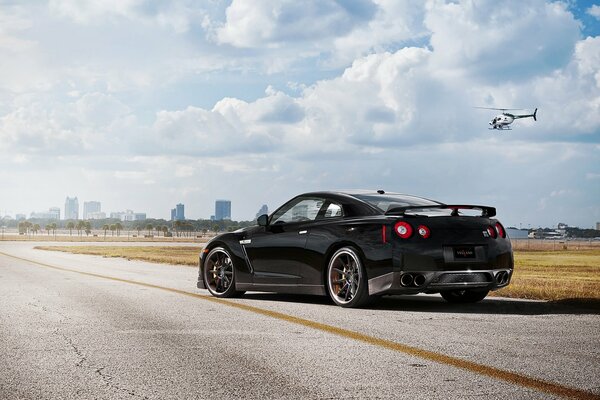 Nissan on the background of an approaching city accompanied by a helicopter