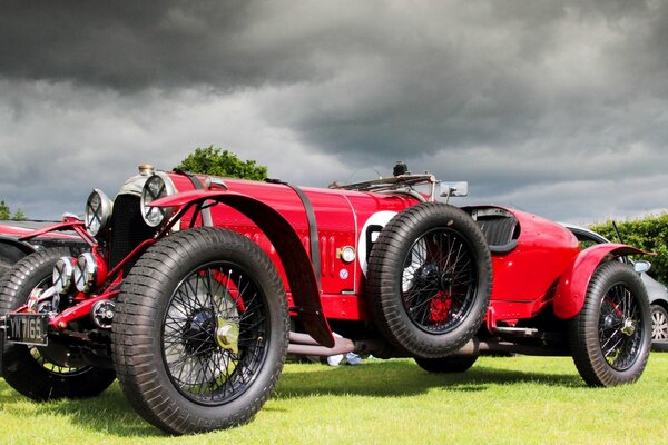 L auto rossa bentley 3 si trova su un erba succosa su uno sfondo di nuvole spesse