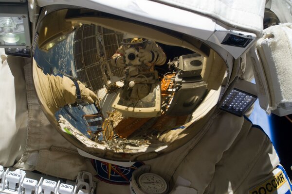 Zwei Astronauten werden im Weltraum durch eine Reflexion am Helm eines Raumanzugs fotografiert