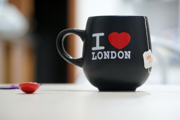 A black mug with tea on a white table with a cloudy background