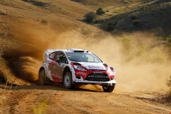 A ford fiesta car rides off-road in clouds of dust