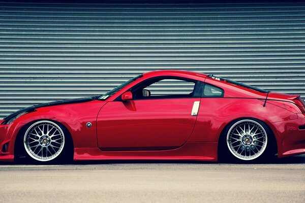 Photo of a red nissan 350z on the background of a closed roller shutter