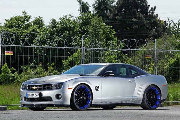 Autoportrait avec une Chevrolet Camaro tuning près de la clôture avec du fil de fer barbelé