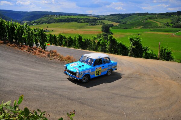 A blue rare car rides on a mountain road against a background of green hills