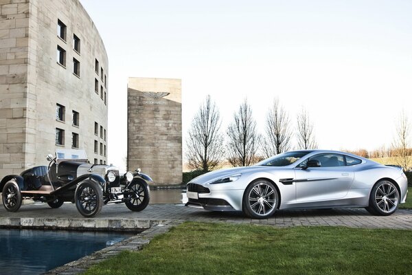 A modern gray car next to a rare one on the background of a concrete building