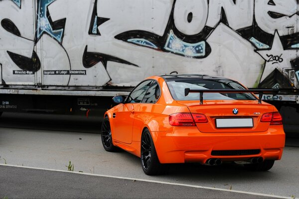 Un BMW coupé naranja contra una pared de fondo con graffiti