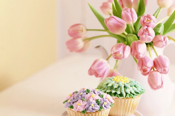 Delicate cupcakes are on the table with a bouquet of tulips in a vase