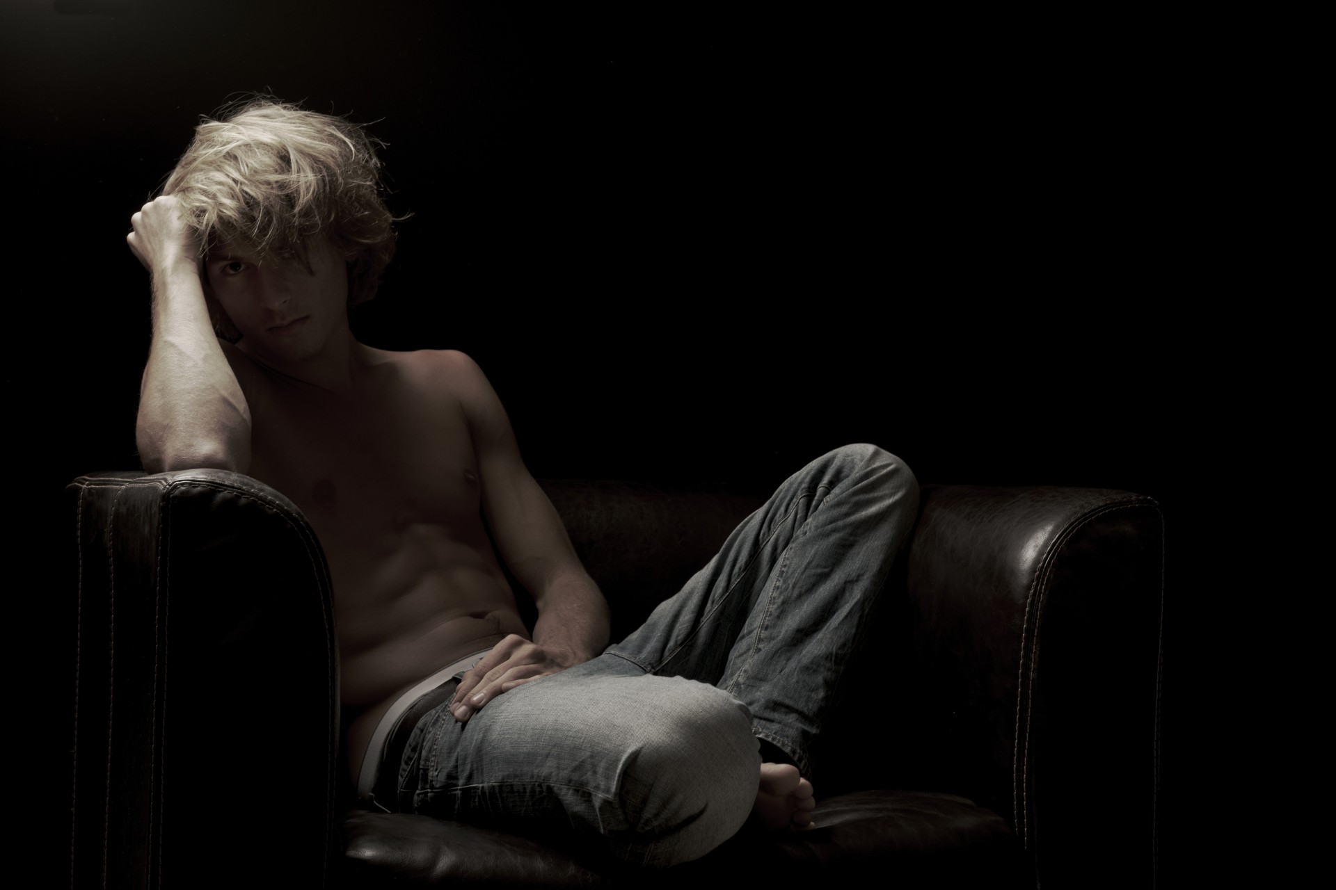 blonde sitting man black background jeans torso chair